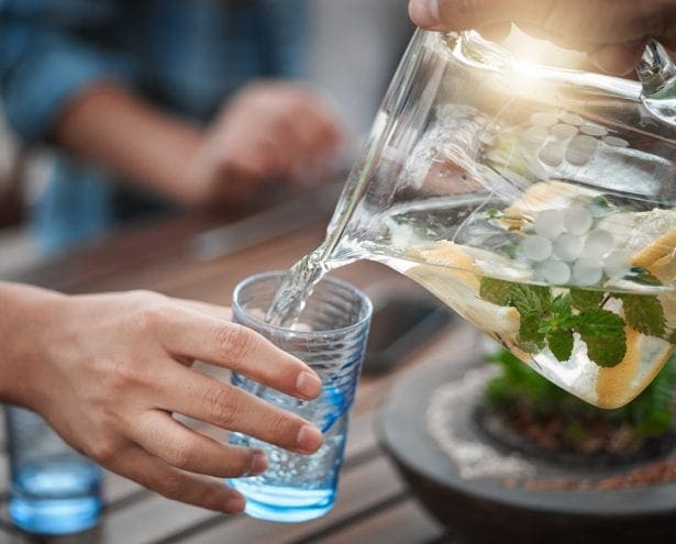 Shot of a unrecognizable person pouring water into a glass outside around a table